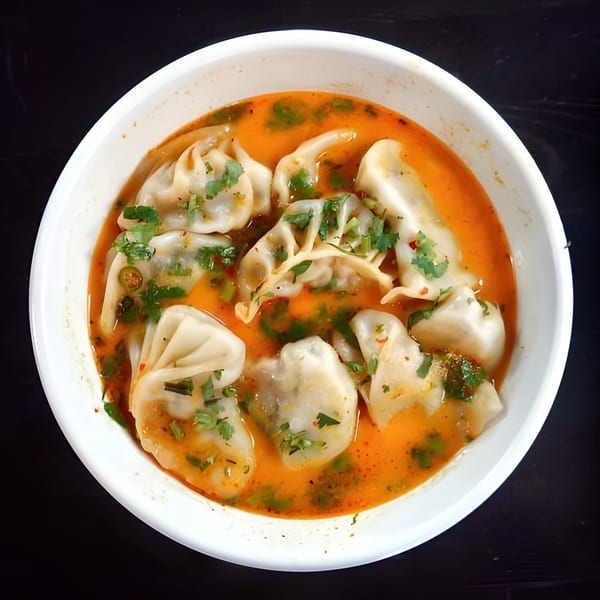 A white bowl of Himalayan Grill momos in a vibrant orange broth, garnished with fresh cilantro.
